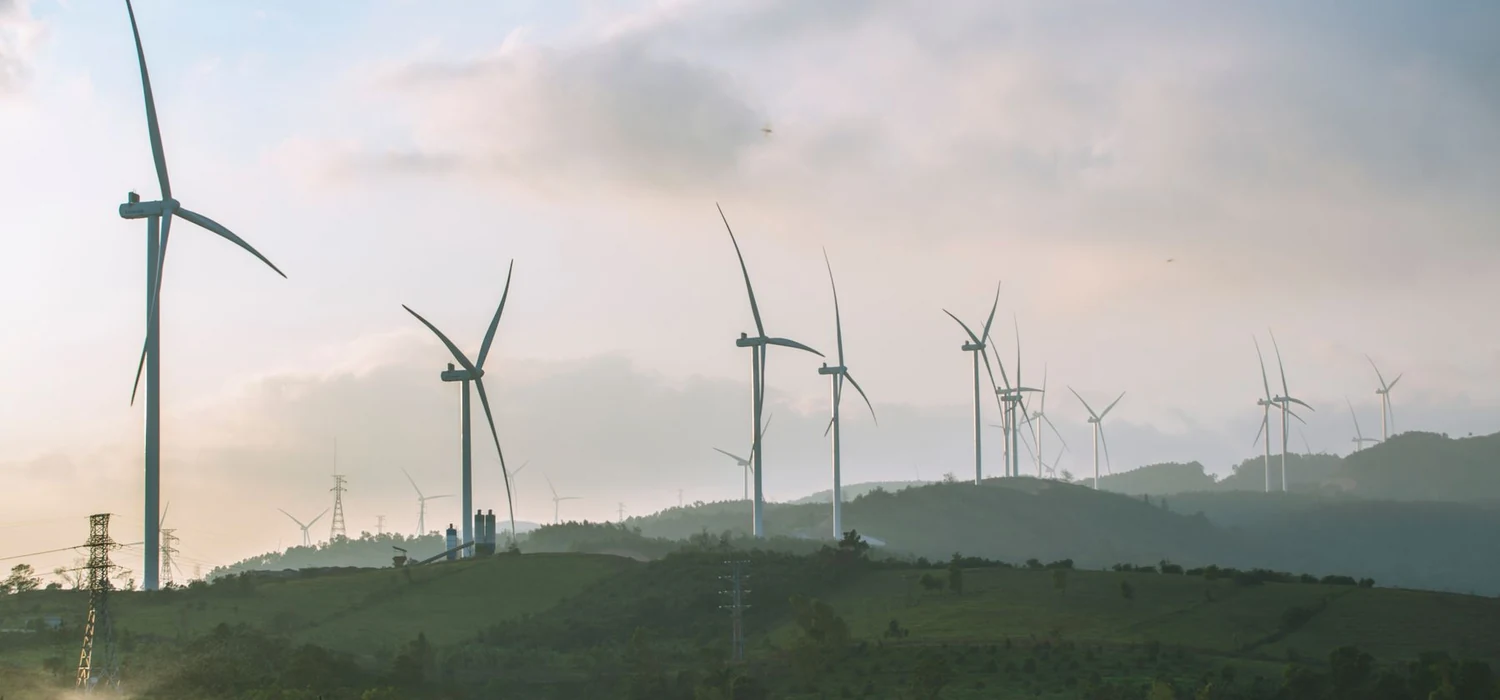 Turbin angin di perbukitan hijau berkabut tipis - foto stok ilustratif, bukan proyek atau dukungan Greenova Energi